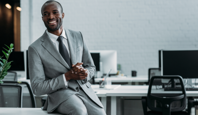 Male financial advisor sitting on desk in office.